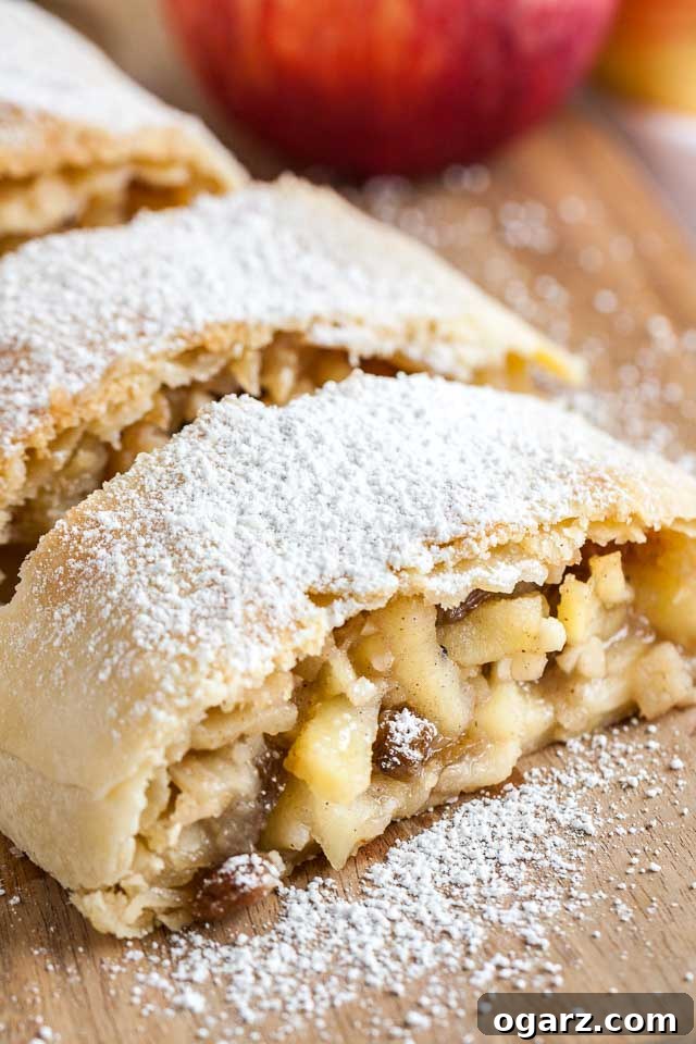 Close-up of several pieces of apple strudel topped with powdered sugar on a wooden cutting board.
