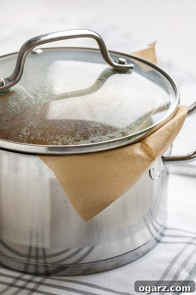 A stainless steel pot, lined with parchment paper, with a fogged-up glass lid.