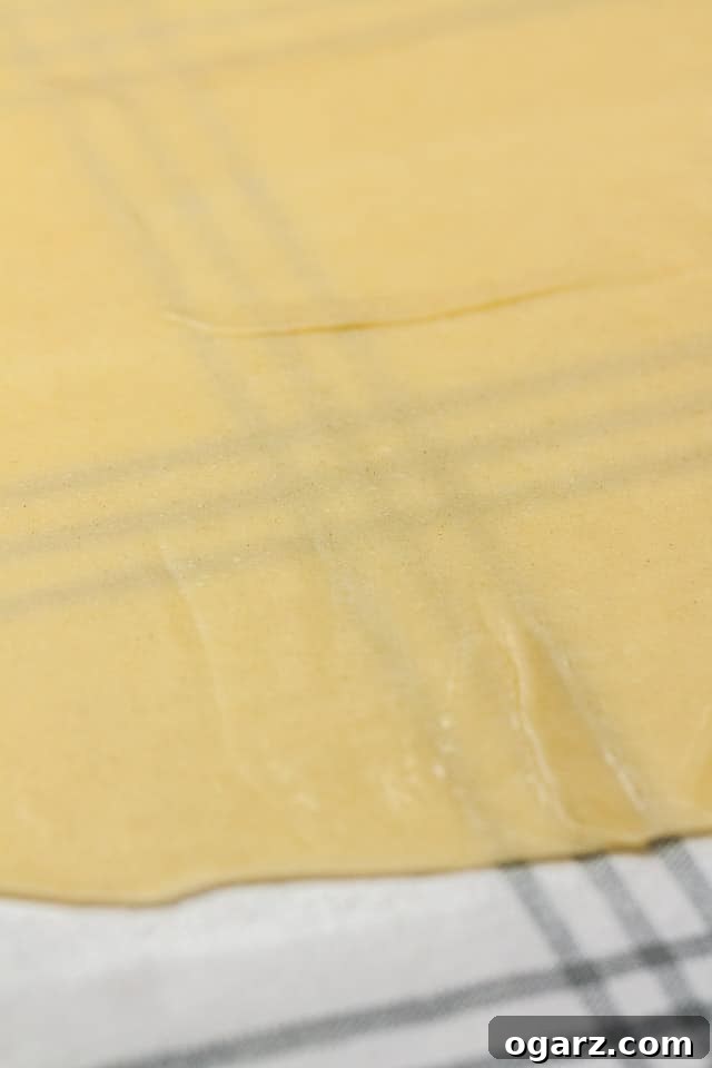Dough for the apple strudel rolled out on a moist dishtowel. The dough is so thin, that the grey plaid pattern of the towel shines through.