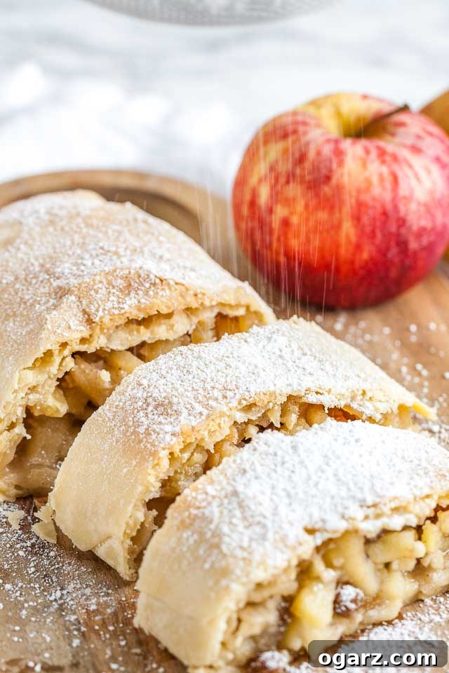 Several pieces of apple strudel topped with powdered sugar on a wooden cutting board with an apple in the background.