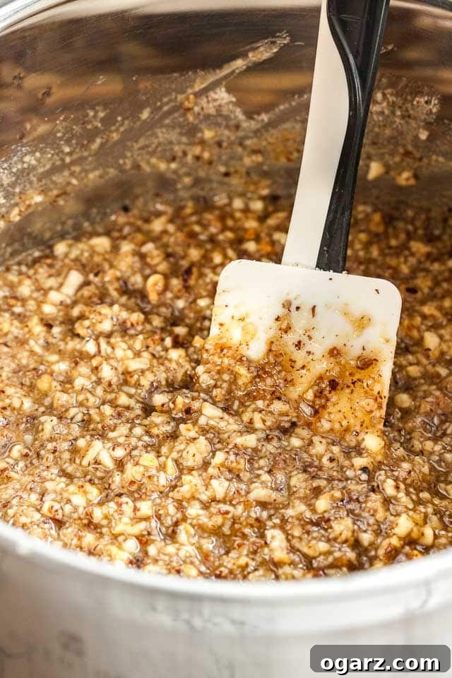 A stainless steel mixing bowl filled with the rich, caramelized hazelnut topping, with a white and black spatula resting within it, ready for spreading.