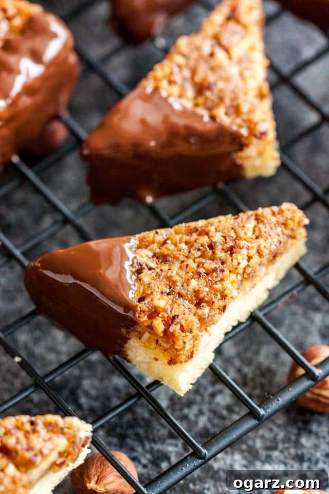 A close-up view of perfectly baked nut corners, one with a chocolate-dipped tip, arranged on a black cooling rack against a dark, inviting background.
