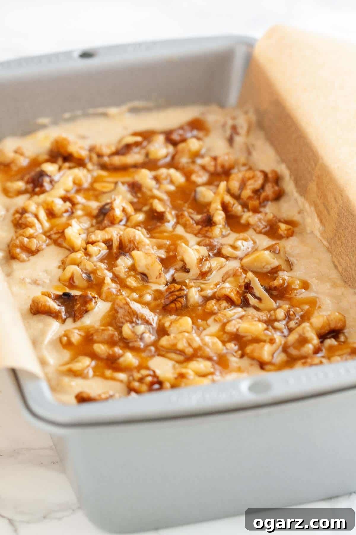 This easy banana nut bread is so moist and delicious! Topped with caramelized nuts and loaded with walnuts and mashed bananas my easy banana bread recipe is a family favorite that tastes great for breakfast or as a snack. A perfect way to use overripe bananas! #bananabread #banananutbread #bananarecipes #bananas #bread #breakfastrecipes A loaf pan, lined with parchment paper, filled with banana nut bread batter, ready for baking, showcasing the rich, thick consistency.