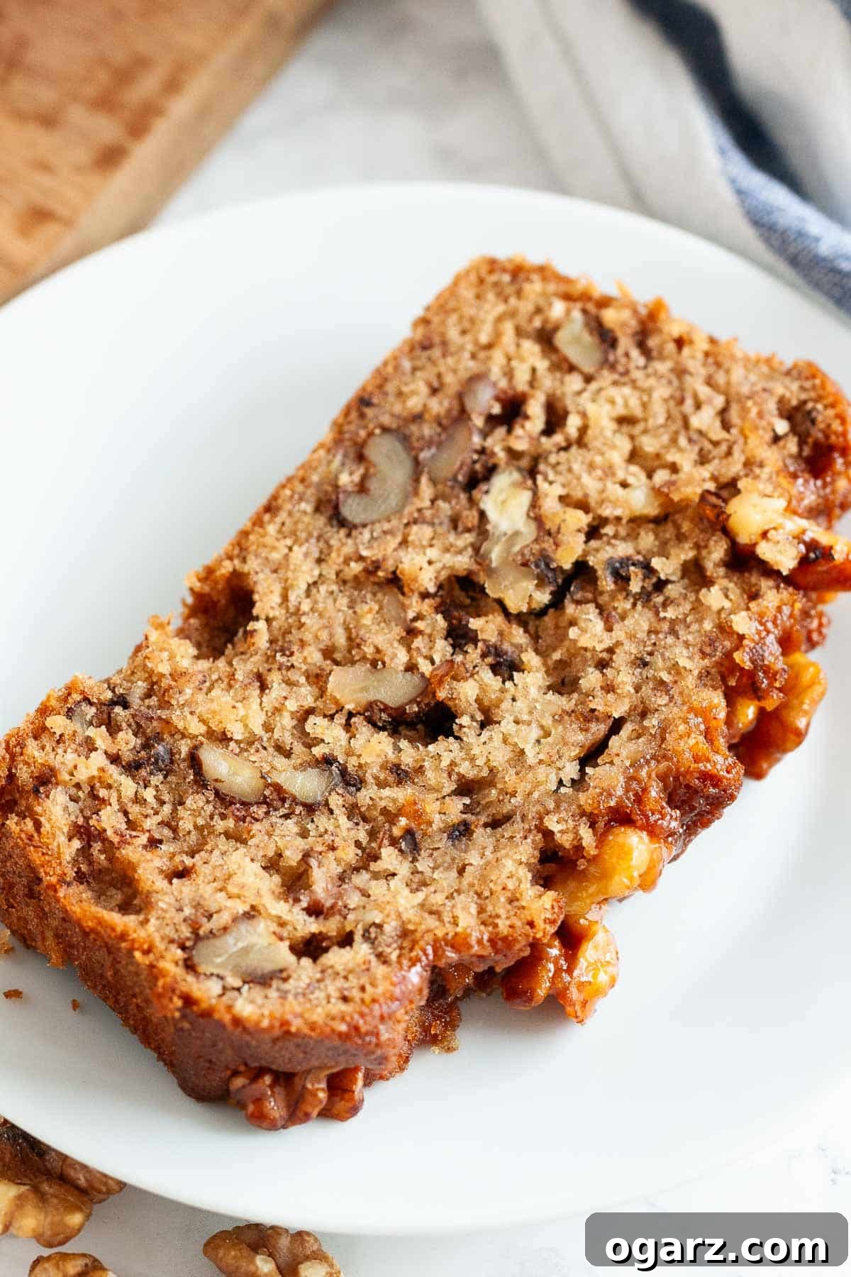 Golden Banana Walnut Loaf 2 A perfectly baked slice of banana nut bread, showing the moist interior, walnuts, and caramelized topping, presented on a simple white plate.