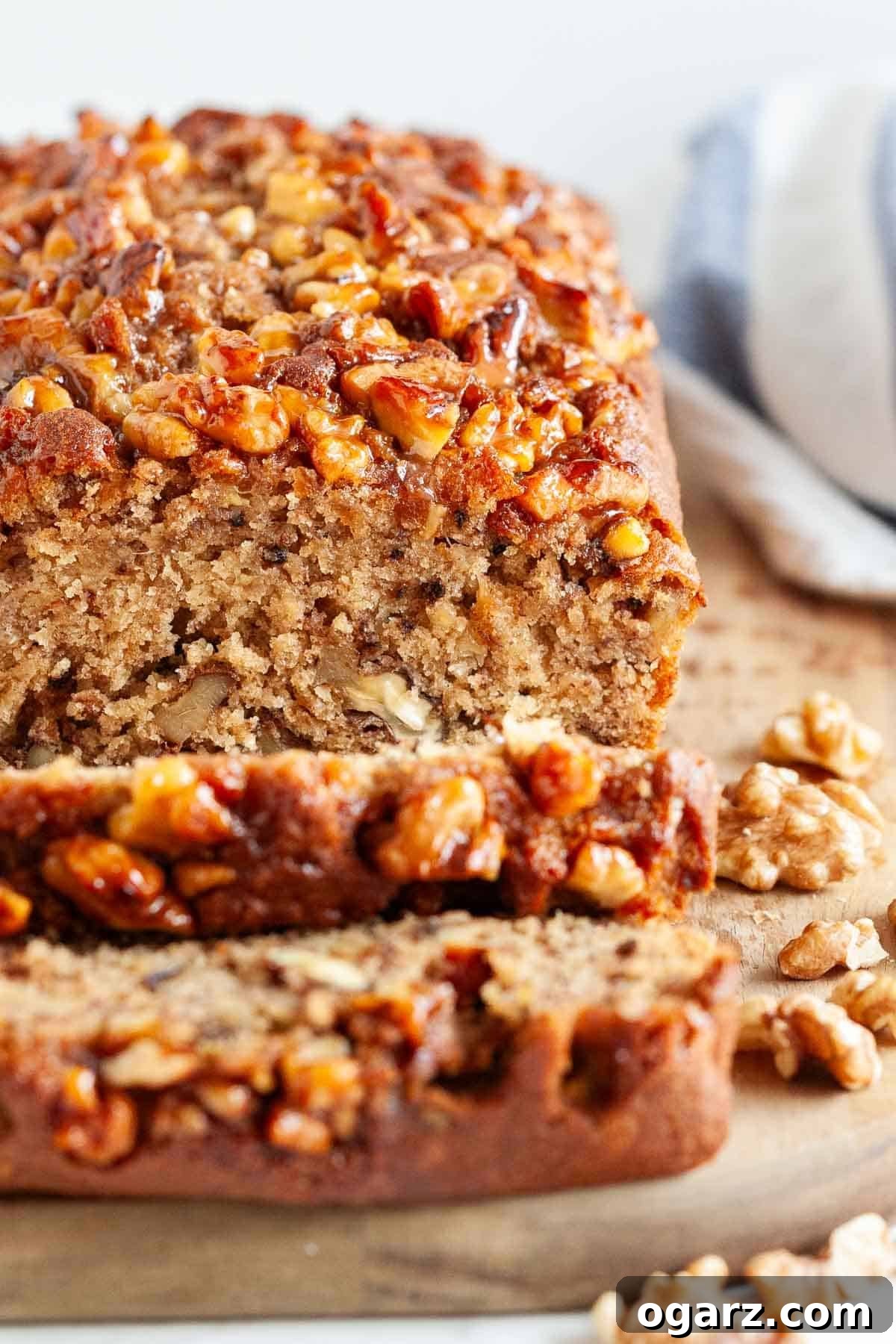 This easy banana nut bread is so moist and delicious! Topped with caramelized nuts and loaded with walnuts and mashed bananas my easy banana bread recipe is a family favorite that tastes great for breakfast or as a snack. A perfect way to use overripe bananas! #bananabread #banananutbread #bananarecipes #bananas #bread #breakfastrecipes A beautifully sliced banana bread displayed on a rustic wooden board, ready to be served, highlighting its rich color and texture.