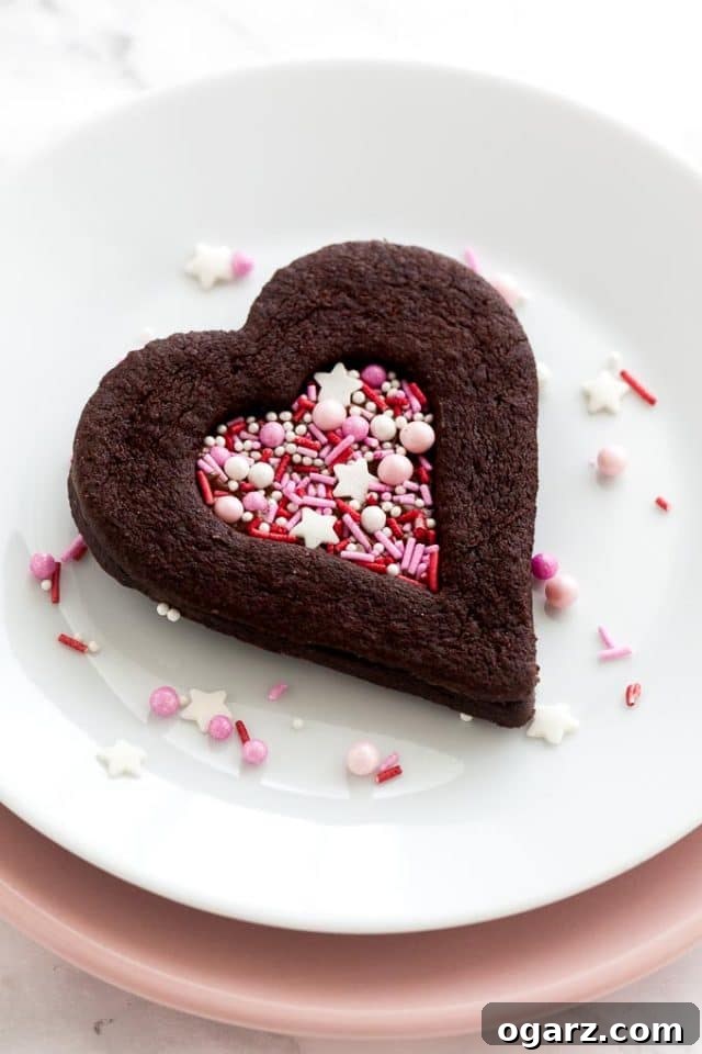 Decadent Chocolate Sugar Cookies 5 A heart-shaped chocolate cookie with a heart-shaped indentation filled with pink sprinkles on a white plate