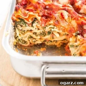 A metal baking pan with spinach lasagna on a wooden cutting board, with a piece removed.