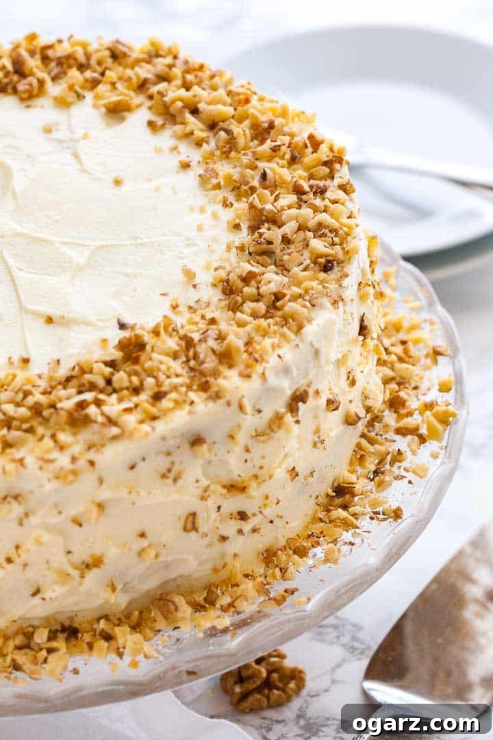 A stunning carrot pineapple cake ready to be served on a beautiful glass dish, perfect for any gathering. #dessert #bakingideas #homemade #partyfood A carrot pineapple cake with walnut pieces on a glass serving dish with a plate and a fork in the background.