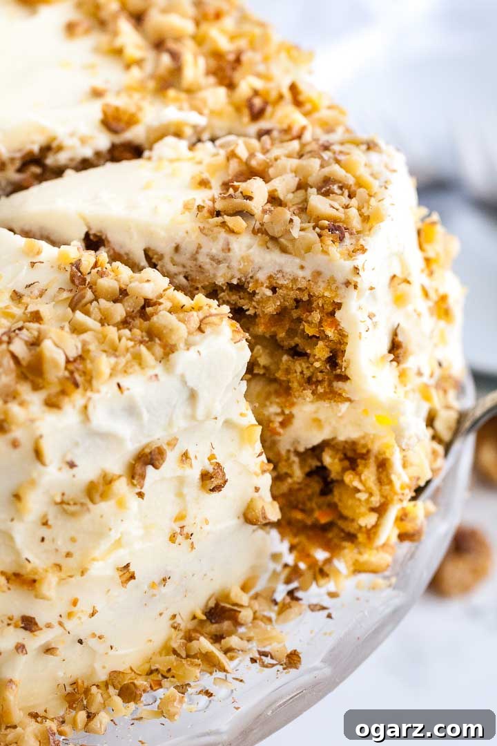 Enjoy a perfectly sliced carrot pineapple cake, showcasing its tender layers and rich cream cheese frosting. #sliceofcake #carrotcakedessert #indulgent A carrot pineapple cake on a glass serving platter. A cake server is lifting out a slice.