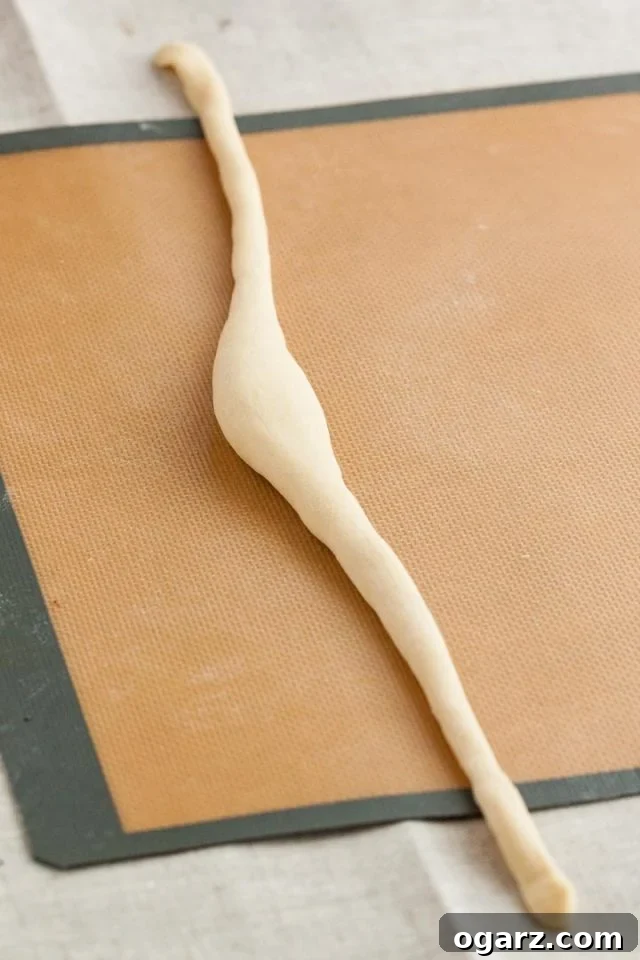 Hearty Bavarian Knots 4 Pretzel dough rolled into a long sausage shape with a thick middle part on a silicone baking mat, illustrating the ideal taper.