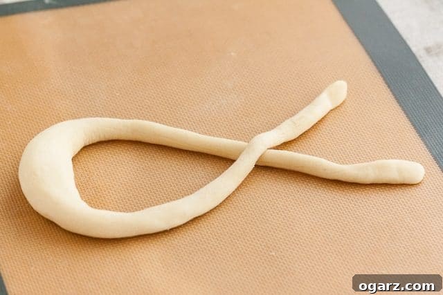 Hearty Bavarian Knots 6 Pretzel dough shaped into a long, tapered ribbon on a silicone baking mat, ready for twisting.