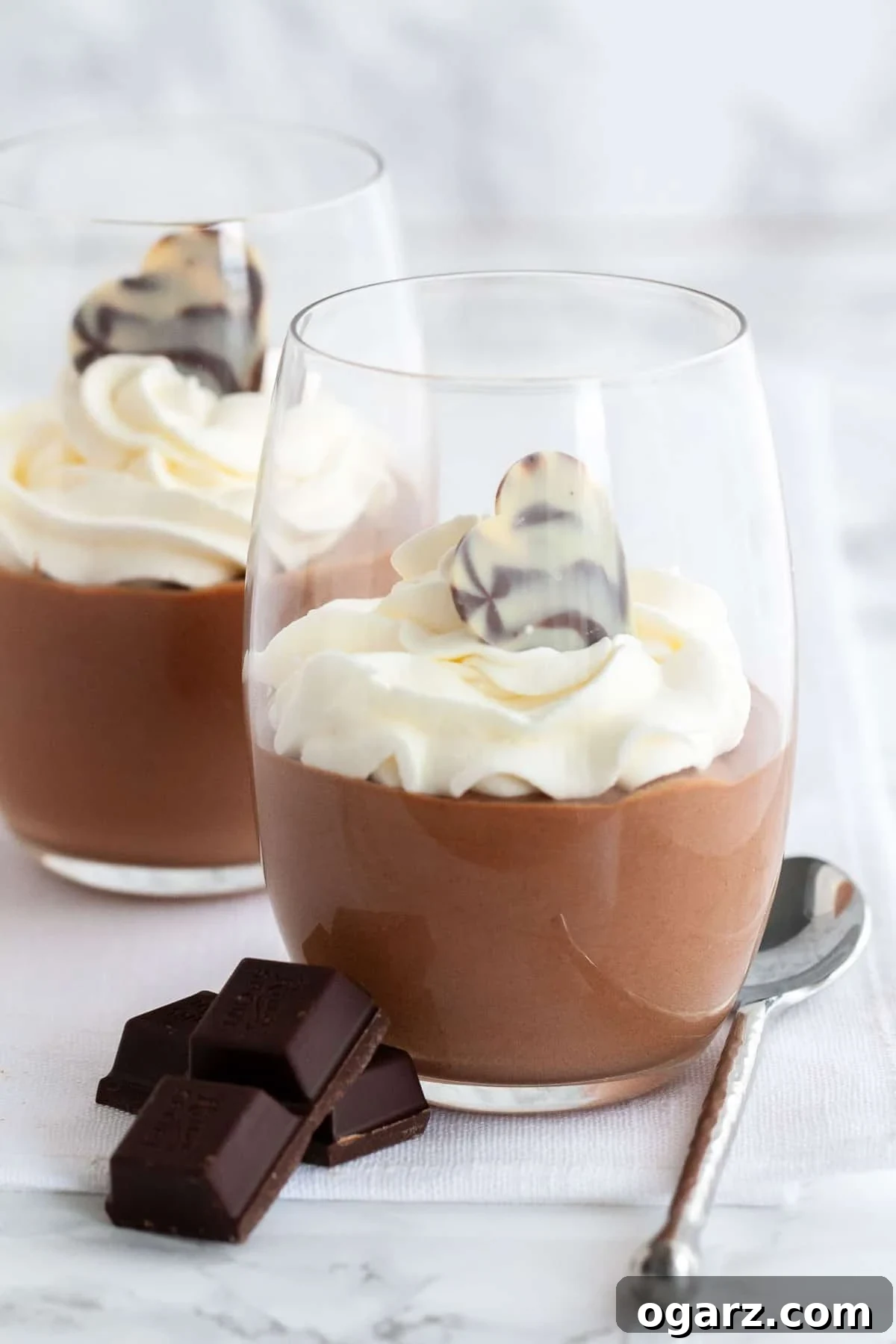 This easy Chocolate Mousse recipe is super simple to make from scratch and deliciously light and fluffy. An eggless mousse recipe that is so airy and chocolatey and can be enjoyed by everyone. It's fancy enough for a party but easy enough to make whenever you have a craving for chocolate! Chocolate mousse in a glass, topped with whipped cream next to pieces of chocolate and a spoon.