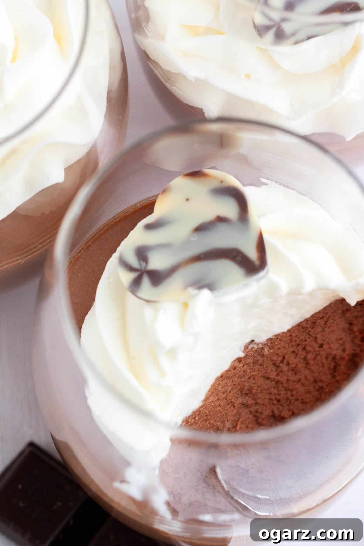 This easy Chocolate Mousse recipe is super simple to make from scratch and deliciously light and fluffy. An eggless mousse recipe that is so airy and chocolatey and can be enjoyed by everyone. It's fancy enough for a party but easy enough to make whenever you have a craving for chocolate! Top-down shot of 3 glasses of chocolate mousse topped with whipped cream.