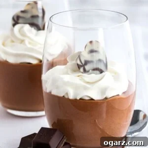 Chocolate mousse in a glass, topped with whipped cream next to pieces of chocolate and a spoon.