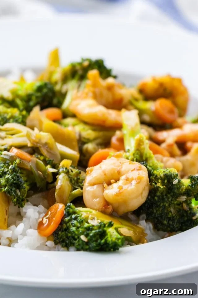 Sticky Honey Garlic Shrimp with Roasted Broccoli 2 A plate of rice topped with shrimp and broccoli stir fry, garnished with sesame seeds.
