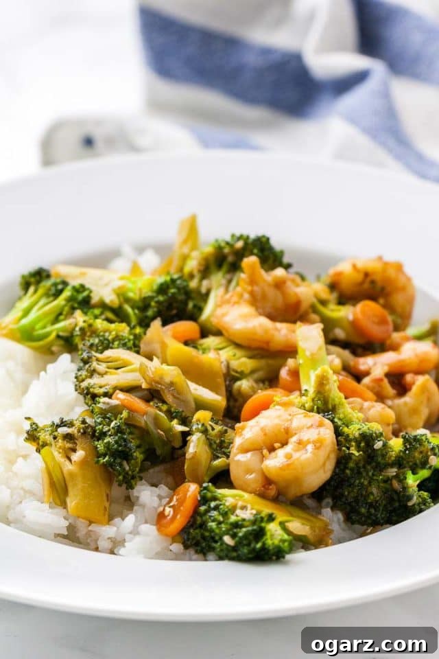 Sticky Honey Garlic Shrimp with Roasted Broccoli 4 A plate of rice topped with shrimp and broccoli stir fry next to a white and blue dishtowel, ready to be served.
