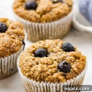 Three banana blueberry muffins on a marble surface next to a white and blue dishtowel.