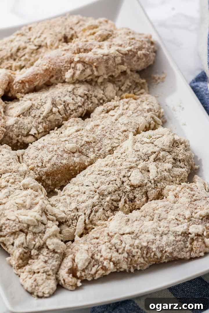 Air Fryer Chicken Tenders are crispy on the outside and juicy on the inside! These homemade breaded chicken strips are marinated in buttermilk to make them extra tender and have a crispy flavorful panko breadcrumb crust seasoned with a KFC-copycat spice mix. A healthier alternative to deep-fried chicken fingers that is perfect for fast food cravings and game day parties! Breaded chicken tenders lying next to each other on a white serving platter.