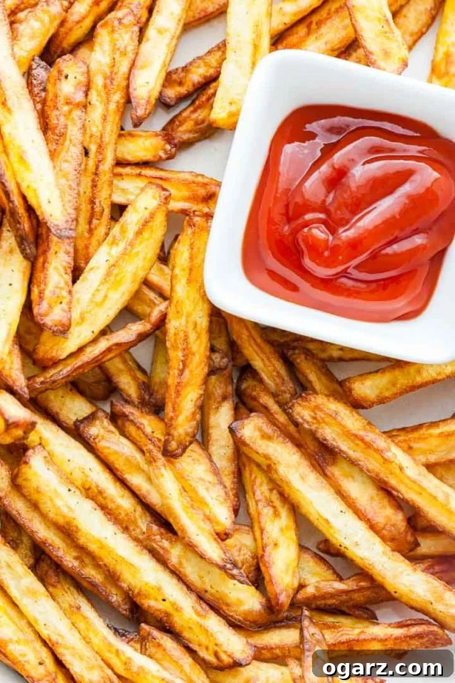 Crispy Air Fryer French Fries: Healthy and Delicious Homemade Fries Top-down shot of golden-brown, perfectly crispy Air Fryer French Fries served in a small, white, rectangular bowl with a side of ketchup.