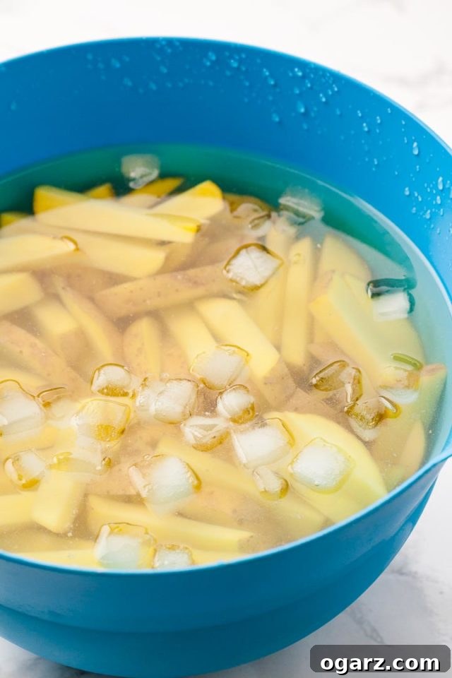 Russet Potatoes Soaking for Air Fryer French Fries A vibrant blue bowl filled with raw Russet potatoes, expertly cut into uniform sticks and submerged in ice-cold water, ready for soaking.