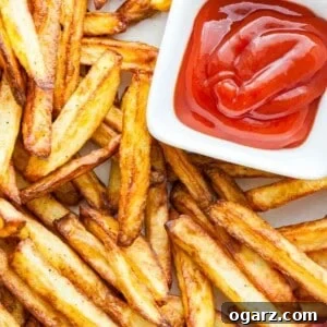 Top-down shot of golden-brown, perfectly crispy Air Fryer French Fries with a small, white, rectangular bowl of ketchup.