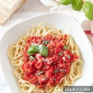 Garden Fresh Tomato Sauce 2 A white plate, with spaghetti topped with tomato sauce, garnished with basil leaves and parmigiano. Next to it, there's basil leaves, a white dish towel with a red stripe and a block of Parmigiano cheese.