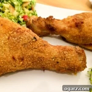 Two breaded chicken drumsticks on parchment paper, with a zucchini salad in the background