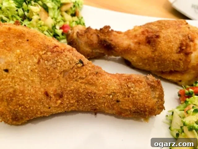 Golden Crispy Air Fryer Chicken 7 Two golden brown, crispy air fryer chicken drumsticks arranged on parchment paper, with a fresh zucchini salad in the background