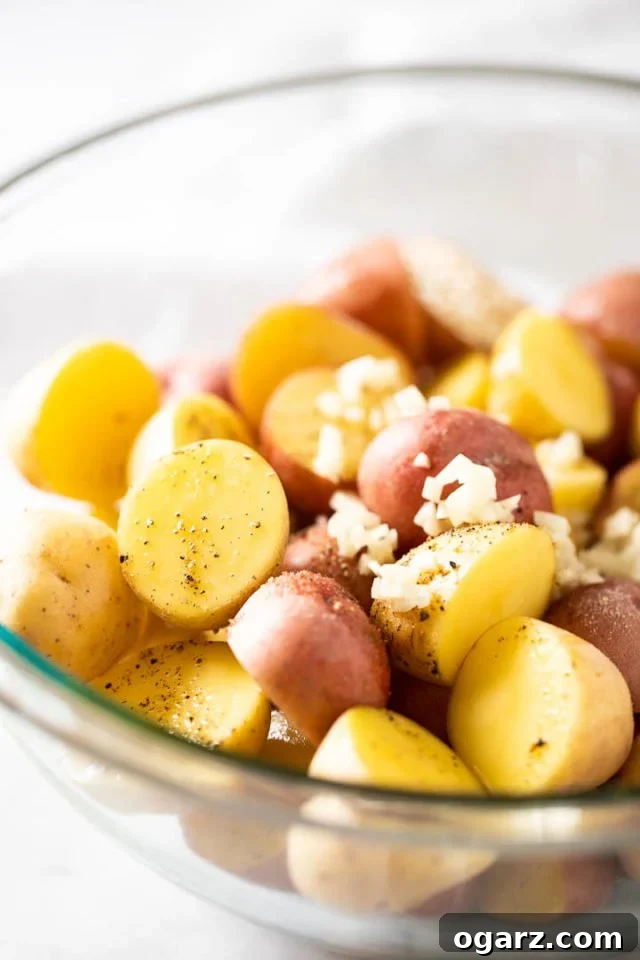 Ultimate Roasted Potatoes 3 Raw, halved young potatoes in a glass bowl, seasoned with oil, salt, pepper, and minced garlic, ready for roasting.