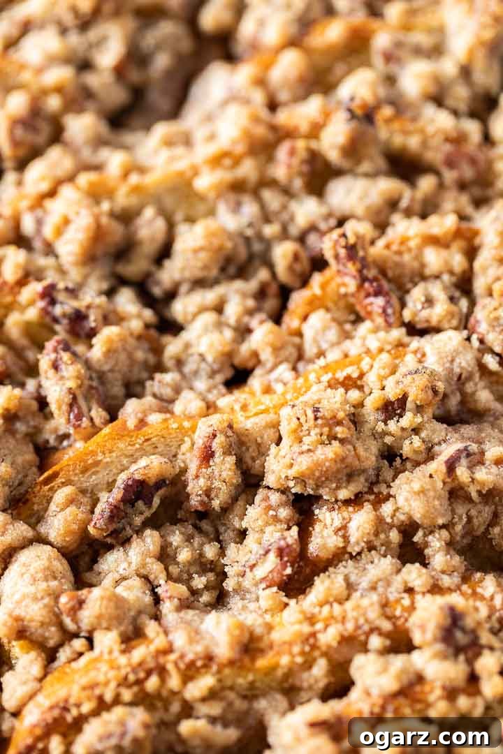 A close-up view of the golden-brown Overnight French Toast Casserole, showcasing its crunchy streusel topping generously studded with pecans and a soft, custardy interior.