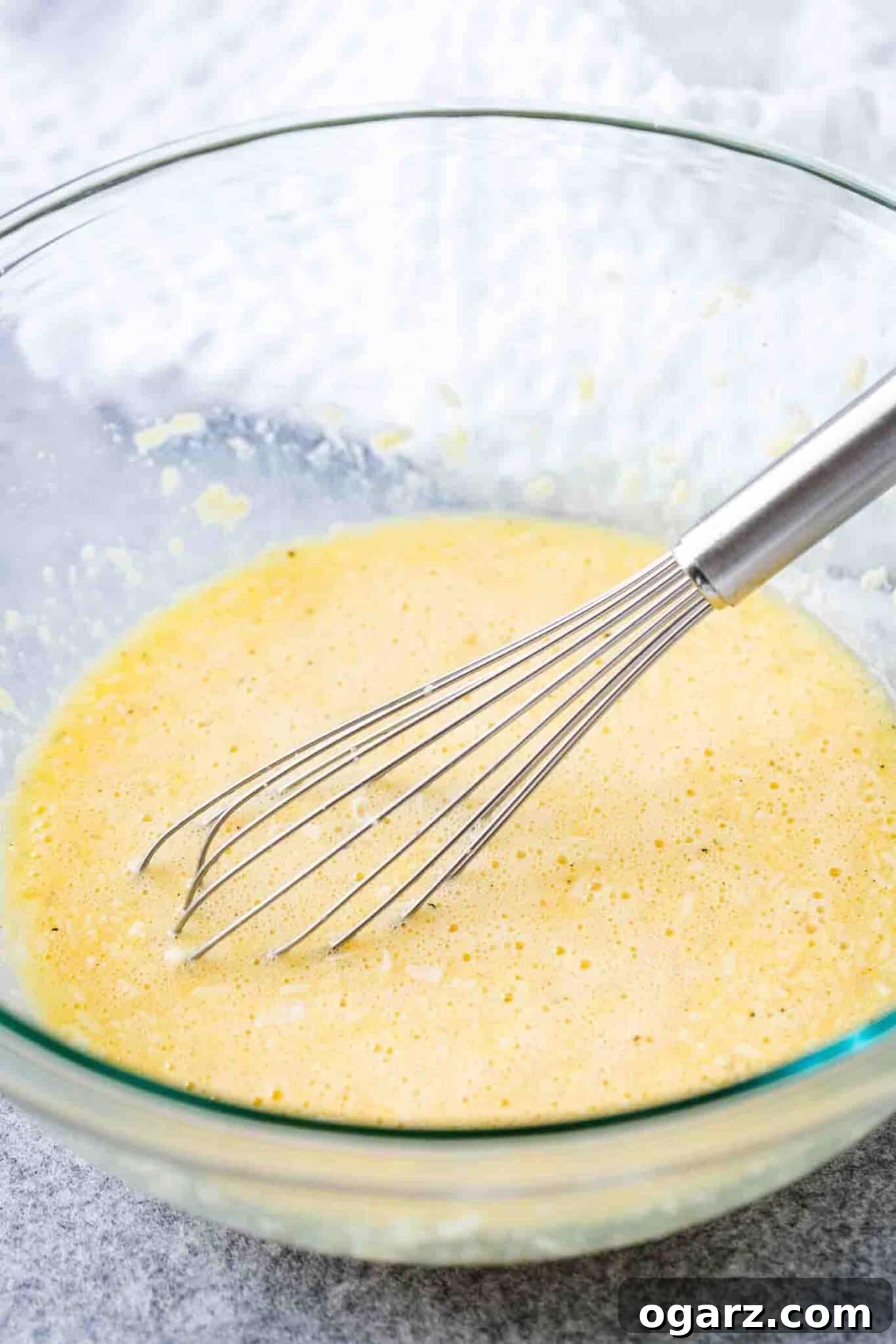 Pasta Carbonara is an easy Italian recipe that can be made in less than 20 minutes from start to finish and is so creamy and delicious. This classic carbonara sauce can be served with your favorite kind of pasta like spaghetti or fettuccine and makes an indulgent and quick weeknight dinner! #pastacarbonara #pastarecipes #spaghetti A glass bowl with a stainless tell whisk containing a mixture of egg and grated parmigiano.