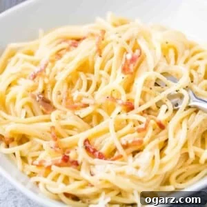 Spaghetti Carbonara on a white plate with a fork in it.