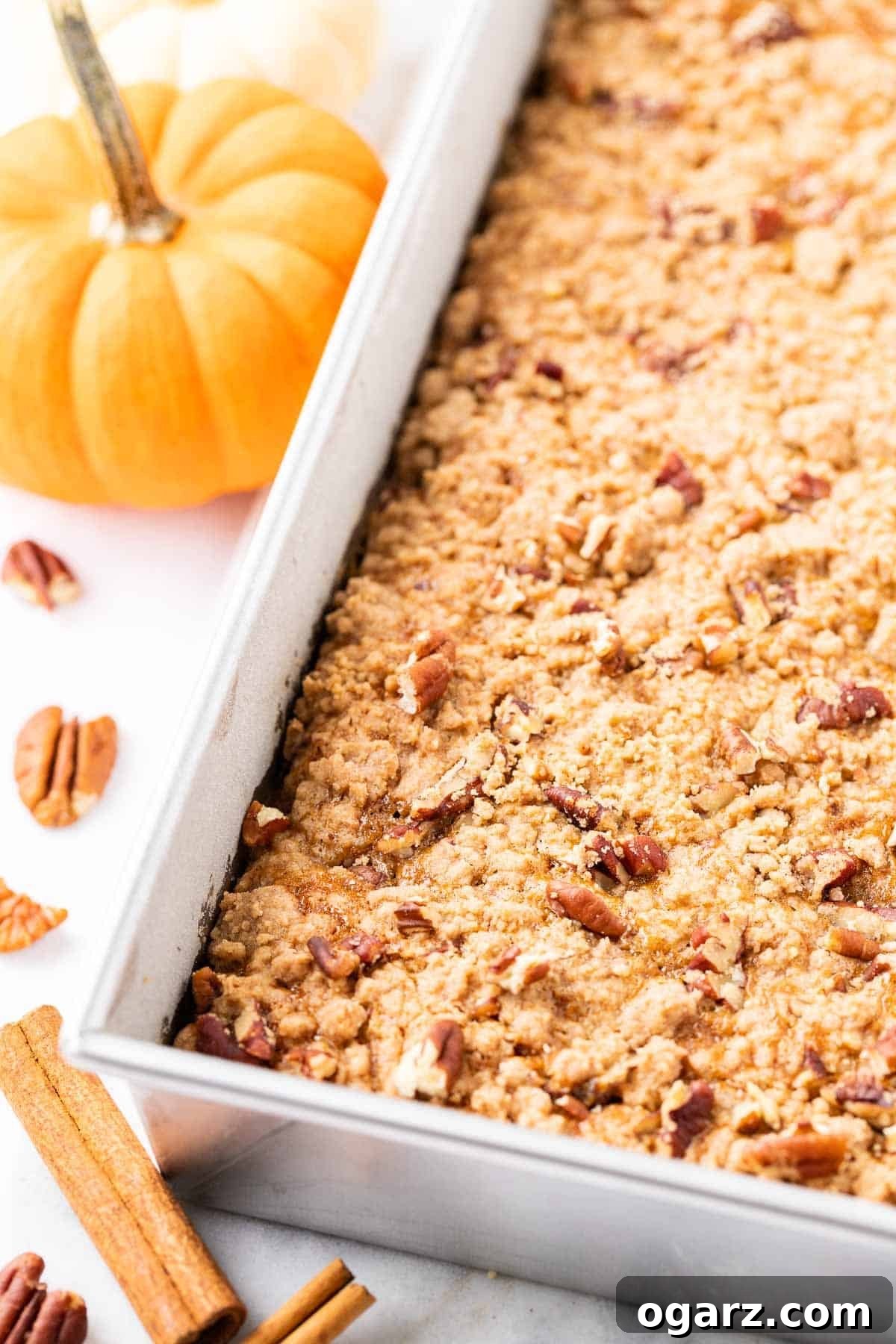 Spiced Pumpkin Crumble Cake 4 A baking pan filled with pumpkin crunch cake, surrounded by whole pecans and a decorative pumpkin.