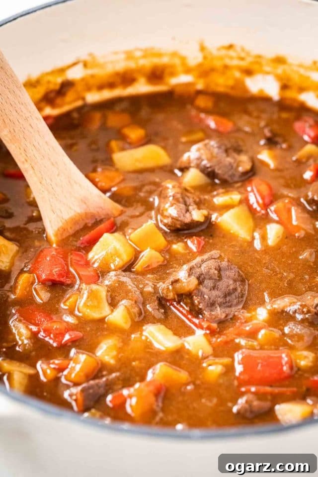 Slow-Cooked Hungarian Goulash in a Dutch Oven A dutch oven with Goulash, containing red peppers, beef and potatoes with a wooden spoon in it, ready to be served.