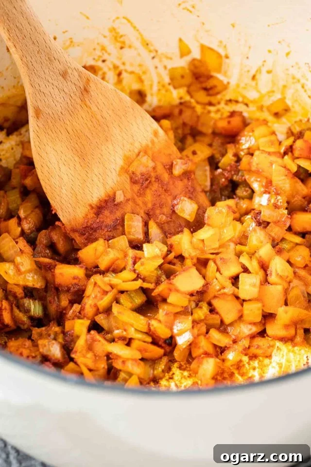 Sautéing Aromatics with Paprika for Goulash A dutch oven with diced onions, carrots, celery and paprika powder being sauteed with a wooden spatula.