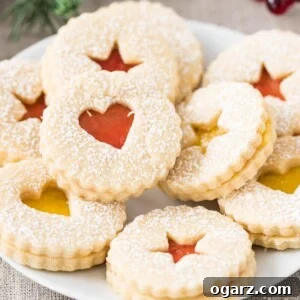 Linzer Cookies stacked on a plate, showing the beautiful jam filling and powdered sugar topping.