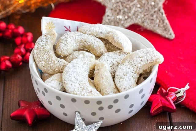 Melt-in-Your-Mouth German Vanilla Crescents 7 A white bowl with silver dots with a napkin, of Vanillekipferl cookies. Next to it, there are several Christmas stars.
