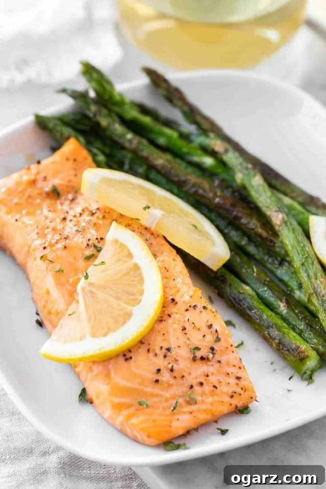 A perfectly cooked piece of air fryer salmon on a white plate, garnished with fresh lemon slices and accompanied by roasted green asparagus.