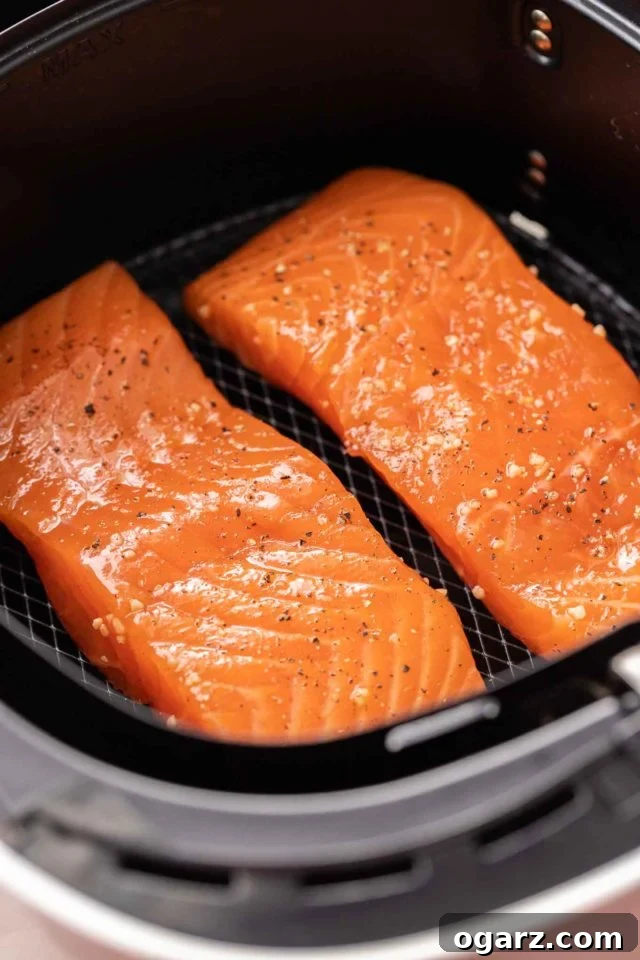 Two salmon fillets, perfectly seasoned with salt and pepper, placed neatly in an air fryer basket, ready for cooking.