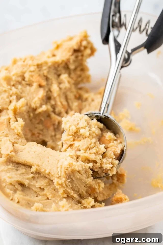 butterscotch cookie dough in a glass bowl being scooped up with a cookie scoop