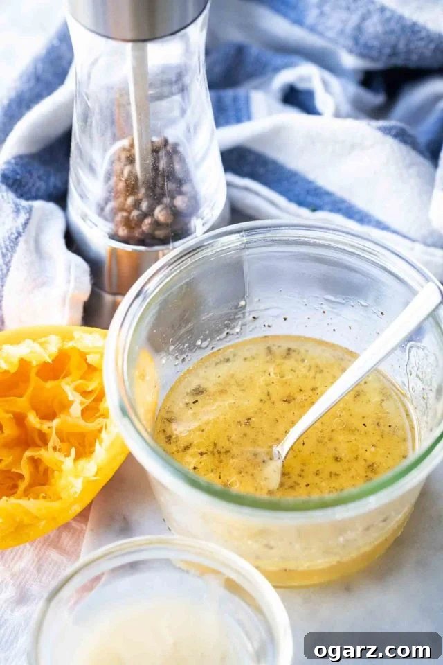 This easy Carrot Salad with Raisins and Apple is a bright and colorful side dish that adults and kids will love! Made with shredded carrots and apples this delicious German Carrot Raisin Salad Recipe can be made in minutes and is loaded with healthy vitamins. #CarrotRaisinSalad #CarrotSalad #SaladRecipes salad dressing in a glass bowl with a spoon in it with a squeezed orange and a pepper mill in the background