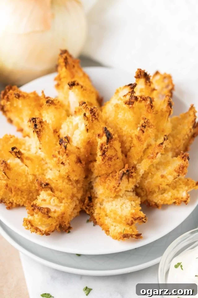 Air Fried Onion Blossom 3 A close-up photograph of a golden and crispy Air Fryer Blooming Onion, perfectly cooked and presented on a white plate, ready for dipping and enjoyment.