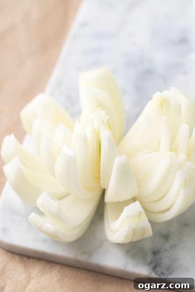 Air Fried Onion Blossom 5 A sweet onion, expertly cut with its petals gently fanned outwards, resting on a sophisticated grey marble surface, demonstrating the ready-to-be-breaded stage.