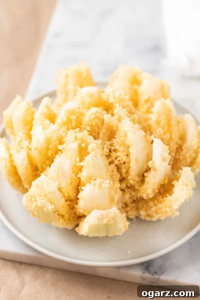 Air Fried Onion Blossom 6 A sweet onion, perfectly cut and with its petals gracefully fanned outwards, now fully coated in a golden breading, prepared and ready to be placed into the air fryer for cooking.