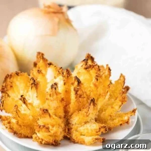 Air Fryer Blooming Onion, a healthier alternative to the deep-fried classic, served on a white plate with dipping sauce.