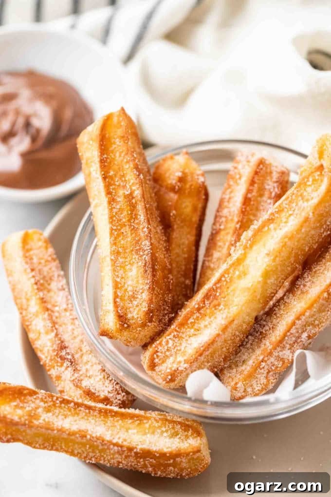 Air-Fried Churro Perfection 2 sugared churros in a glass bowl with parchment with a small white bowl of nutella in the background
