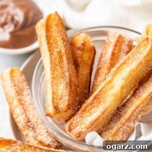 sugared churros in a glass bowl with parchment with a small white bowl of nutella in the background