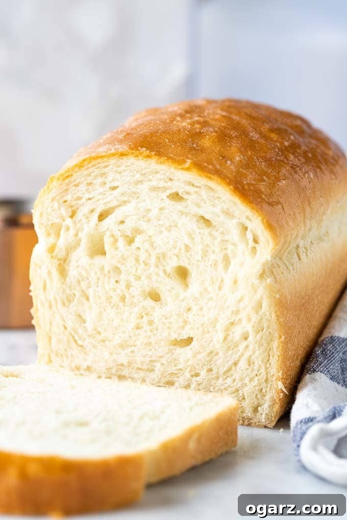 The Unvarnished Truth About White Bread 2 A perfectly baked white bread loaf with the first slice cut off, resting next to a white and blue dish towel.