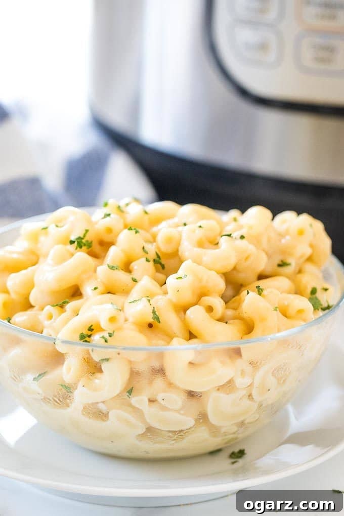Mac and Cheese in a clear glass bowl, garnished with parsley, with an Instant Pot visible in the soft-focus background