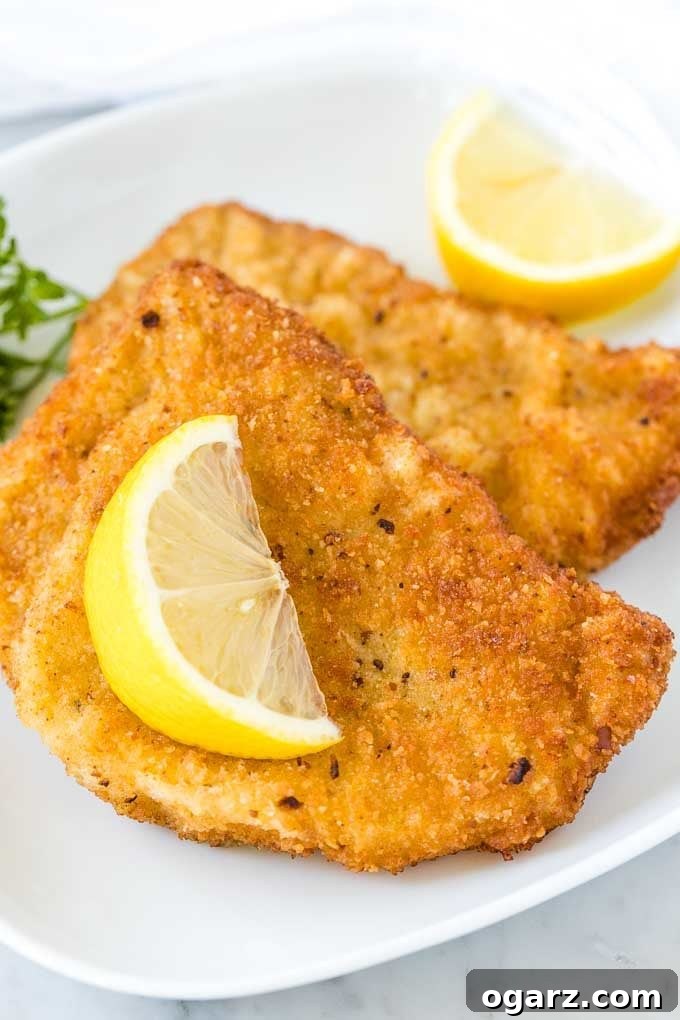Two fried Schnitzels on a white plate, garnished with a wedge of lemon and parsley
